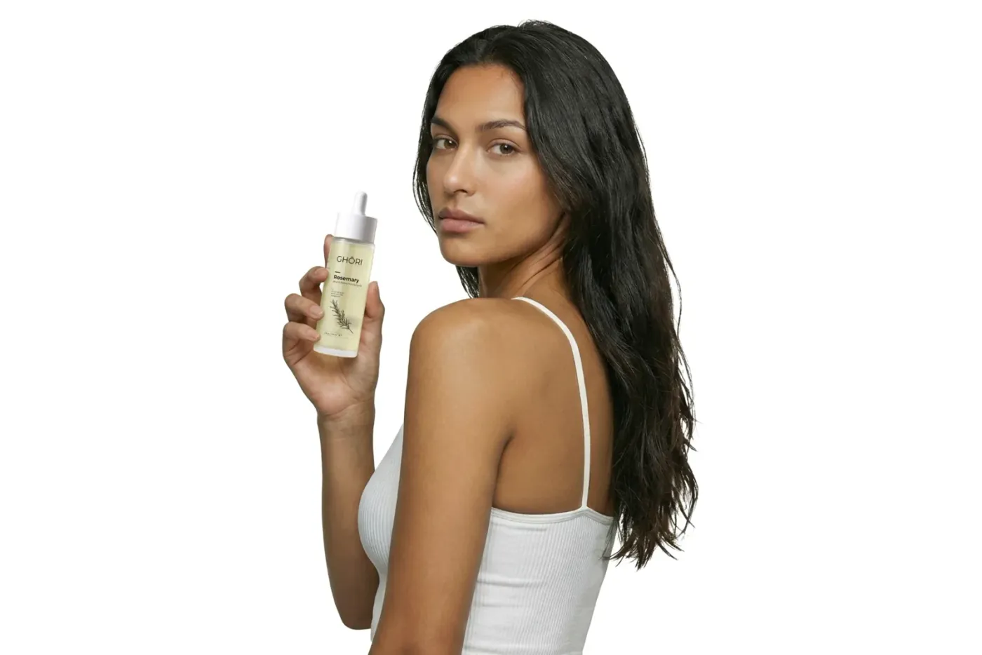 Dark-haired model looking over her shoulder while holding the Ghori® Rosemary Mint & Biotin Oil dropper bottle